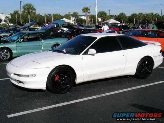 White 1993 Ford Probe coupe with black wheels and red brake calipers, parked at an outdoor car show