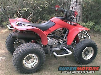 Red 2005 Honda TRX 300 EX ATV with black seat and exhaust, parked on grass near trees