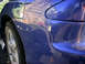 1993 Ford Probe - Damage to the rear quarter panel of a blue car, with paint peeling near the wheel.