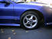 1993 Ford Probe - A close-up view of the front wheel and fender of a blue 1993 Ford Probe, with fallen leaves scattered on the ground.
