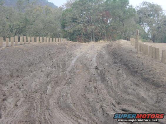Muddy track with wooden posts and trees in background