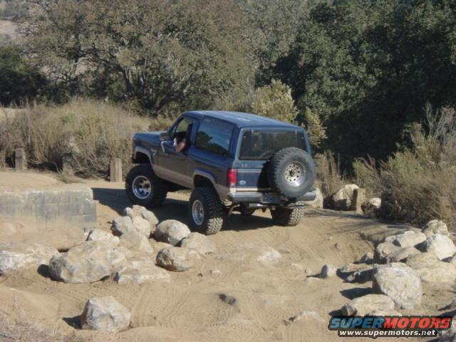 Blue SUV with spare tire on rear, driving over rocks on a dirt path