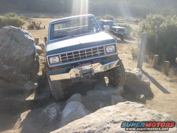 Green Ford Bronco II navigating rocks, front view. Winch attached to bumper