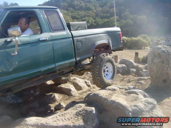Green pickup truck with lifted suspension driving over large rocks