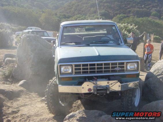 Green 1986 Ford Bronco II off-roading over rocks with another truck behind it