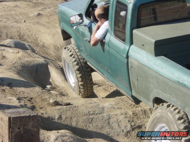 Green pickup truck with large tires driving on a dirt track