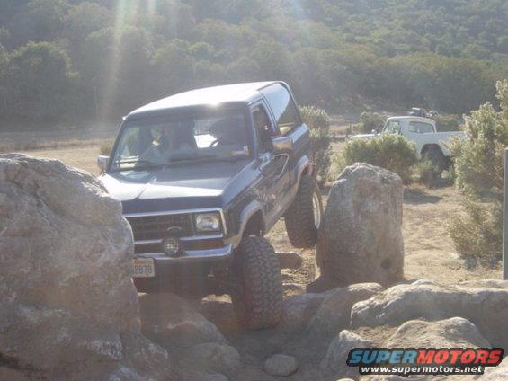 Dark blue 1986 Ford Bronco II off-roading over rocks, with another vehicle in the background