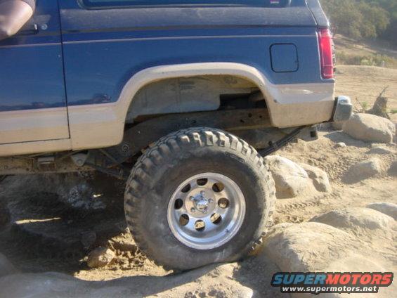 Blue and tan SUV's rear wheel on rocks, showing off-road tires and suspension