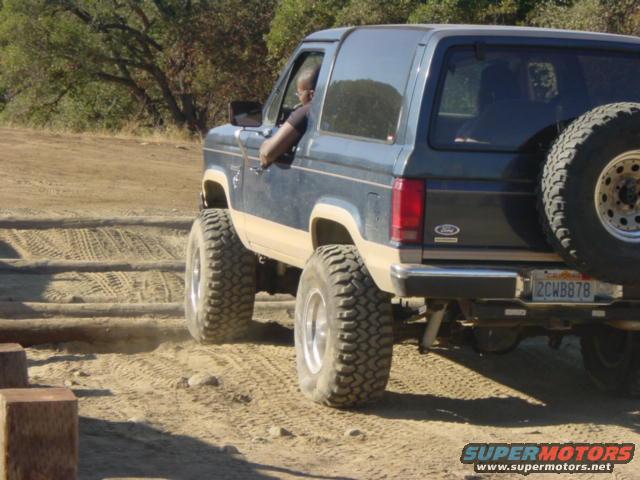 Dark blue and tan Ford Bronco II with off-road tires driving on a dirt path