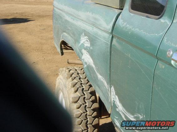 Green pickup truck rear quarter panel with white scratches and large off-road tire