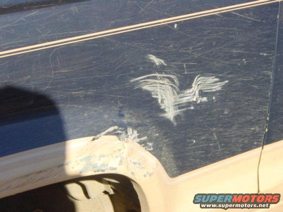 Close-up of a dark blue vehicle body panel with white paint scratches and a damaged wheel well area