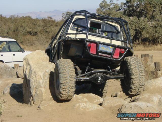 Buggy with roll cage going over rocks, white SUV nearby