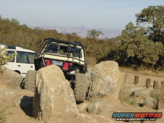 Off-road vehicles on rocky terrain; one is a white van, the other is a modified SUV with a roll cage