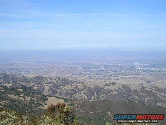 View from a hilltop overlooking a valley with a town in the distance under a hazy sky