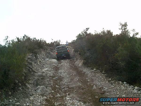 Green pickup truck on a rocky, off-road trail with brush on either side
