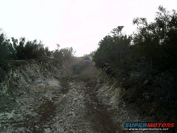 Off-road vehicle driving up a rocky, overgrown path