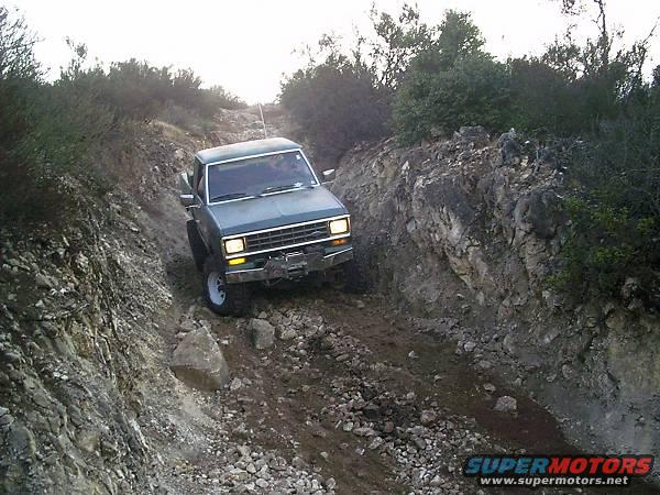 Truck going down a steep, rocky path with bushes on the sides