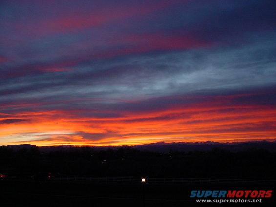 Sunset sky with vibrant orange, red, and purple clouds over a dark, silhouetted mountain range and landscape