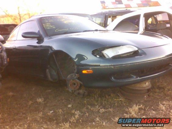 Dark green coupe with missing front wheels, headlights damaged, sitting on tires