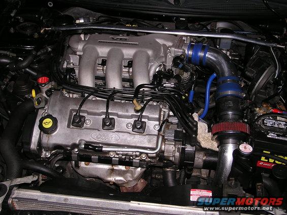 Ford V6 engine with aftermarket intake and strut bar. "Ford" and "V6 DOHC" visible
