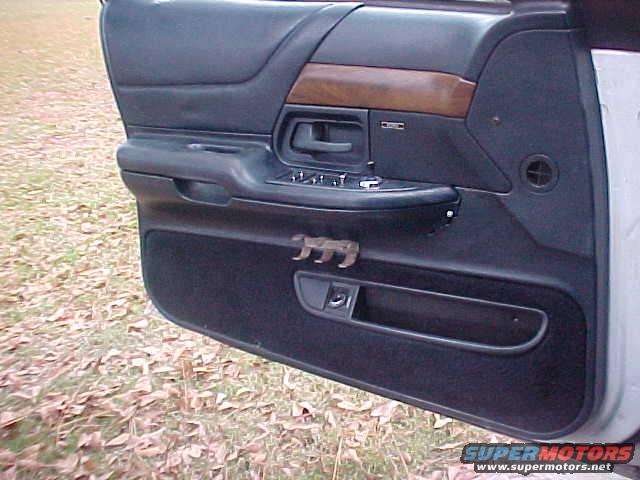 car door panel with wood trim, window controls, and a small bear figurine on the armrest