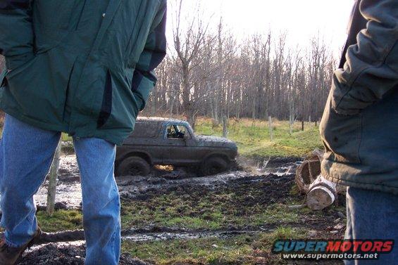 Muddy SUV stuck in a muddy field with two people watching