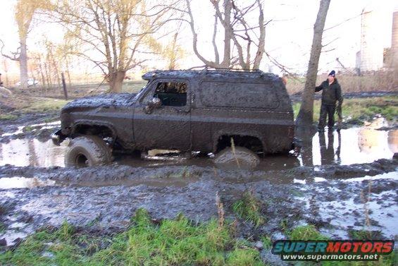 Mud-covered SUV stuck in mud, side view, with a person standing nearby