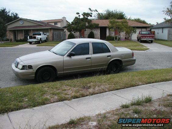 Gold Ford Crown Victoria parked on street, white pickup and red Ford pickup in driveways