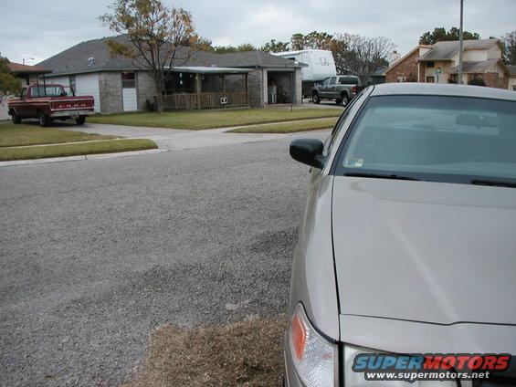 Tan sedan front corner, with a red pickup and a gray truck visible in background