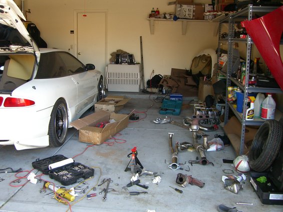 White coupe with trunk open, disassembled exhaust system on floor