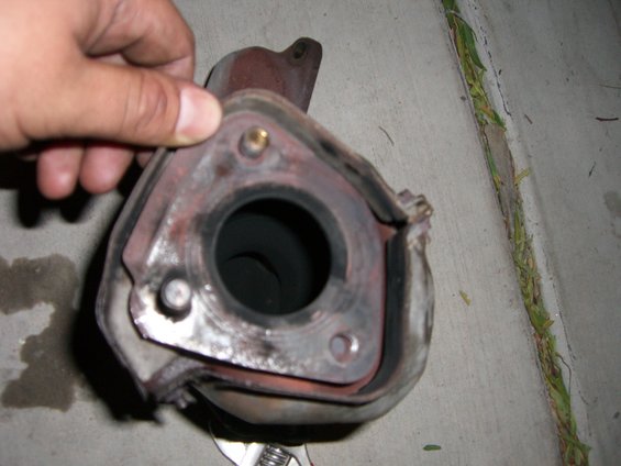 Hand holding exhaust pipe flange with mounting bolts visible