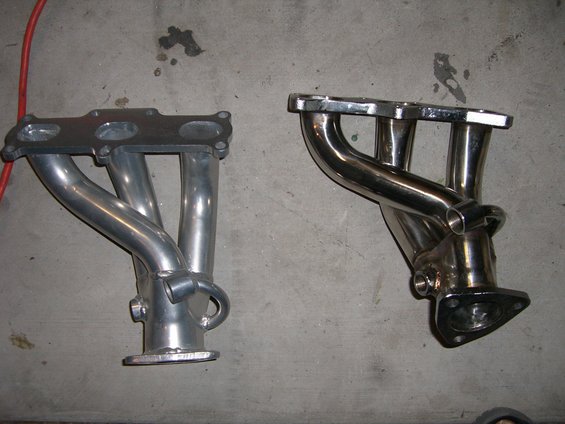 Two exhaust manifolds, one aluminum and one chrome, on a concrete floor