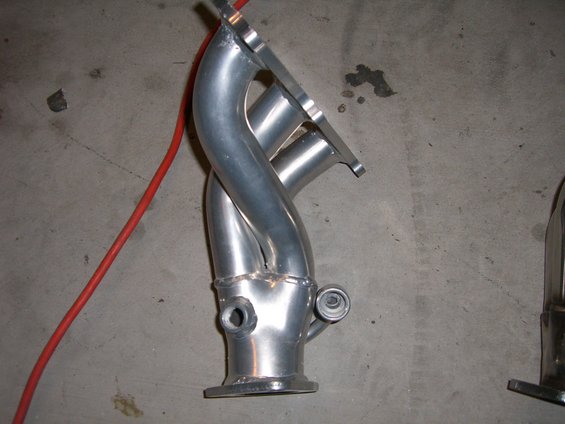 Aluminum exhaust manifold with four pipes merging into one, on a concrete floor