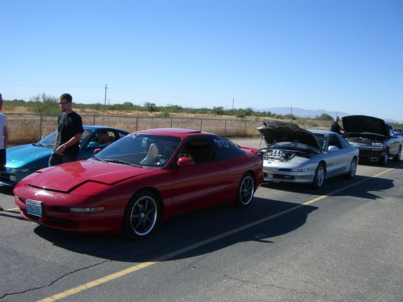 Red coupe with pop-up headlights and aftermarket wheels parked on asphalt