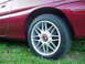 1993 Mazda MX-3 - A close-up shot of a car's wheel and fender, with grass visible below.