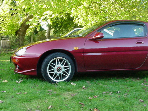 Side view of a red 1993 Mazda MX-3 parked on grass