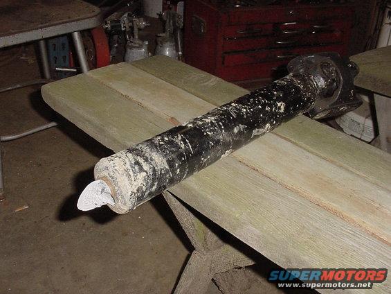 Driveshaft with white protective cap on one end, resting on wooden planks