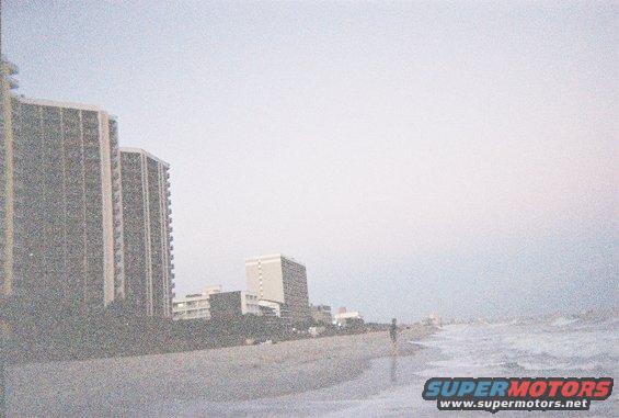 Beach with ocean waves, sand, and distant buildings under a hazy sky
