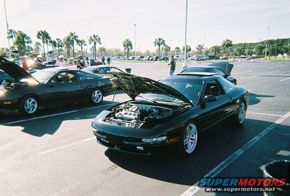 Black coupe with hood open, showing engine, parked in lot with palm trees