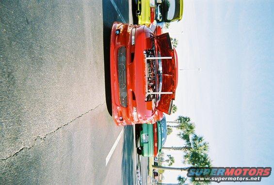 Red sports car with hood open, parked next to a green car and a yellow car