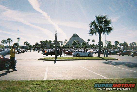 Parking lot scene with multiple cars, palm trees, and a large pyramid building in the background
