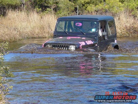 Black Jeep Wrangler with pink "TIN GIRL" decal driving through water