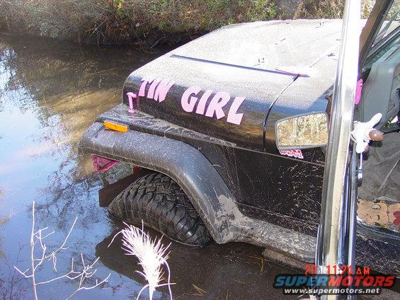 Black Jeep Wrangler partially submerged in water, with pink 'TIN GIRL' lettering on the hood