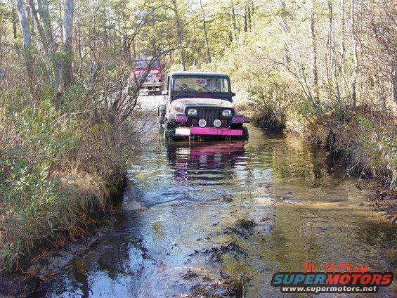 Dark Jeep Wrangler with pink bumper driving through water