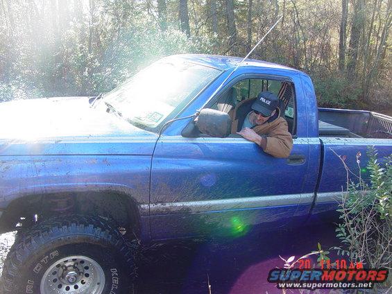 Blue pickup truck stuck in mud, driver wearing a 'Police' hat