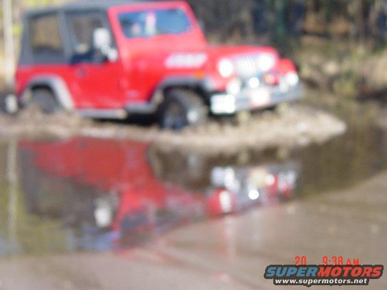Red Jeep Wrangler driving through mud and water