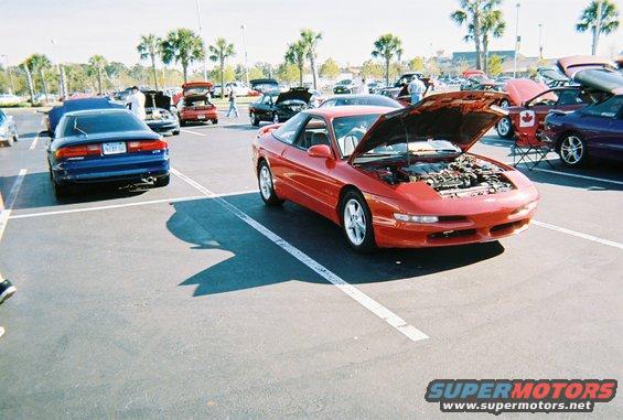 Red sports coupe with hood open, parked in a lot with other cars