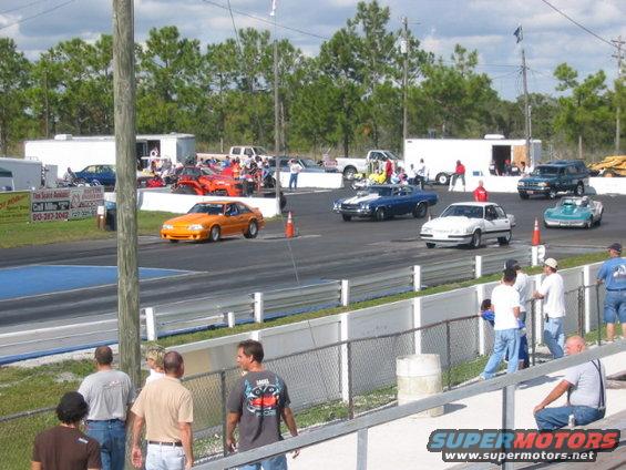 Drag strip with an orange Mustang, blue Chevelle, white sedan, and teal convertible