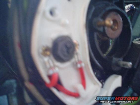 Close-up of red wires connected to a screw terminal inside a white plastic housing, with black plastic and metal components visible