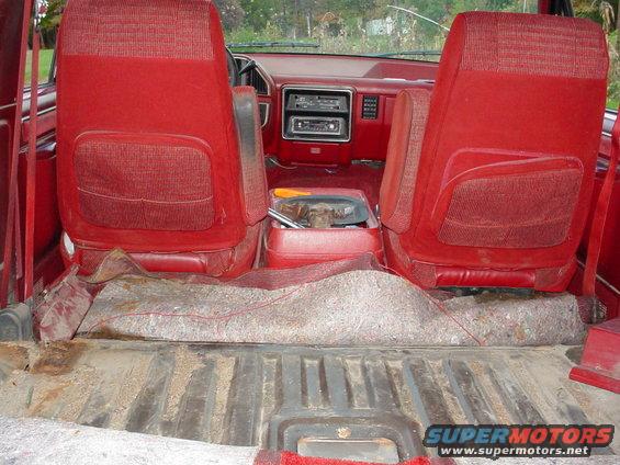 Interior of a red SUV with front bucket seats and a center console. The rear cargo area has a carpeted mat over the floor